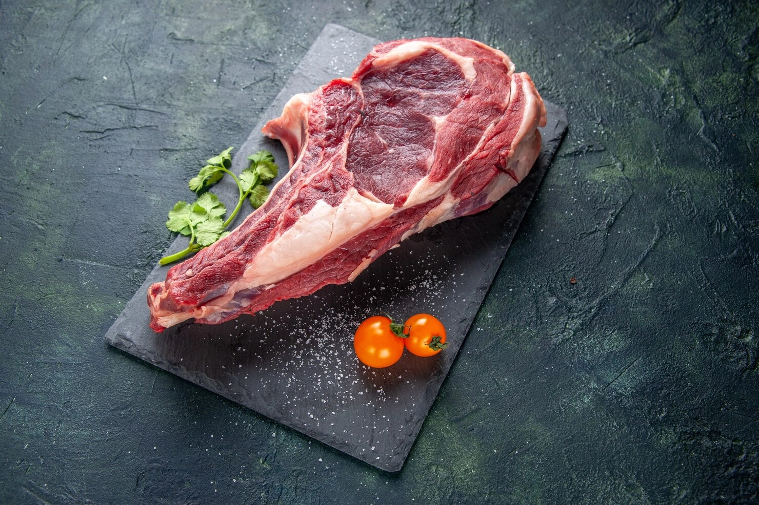 Raw bone-in steak on a slate board with cherry tomatoes Raw bone-in steak on a slate board with cherry tomatoes